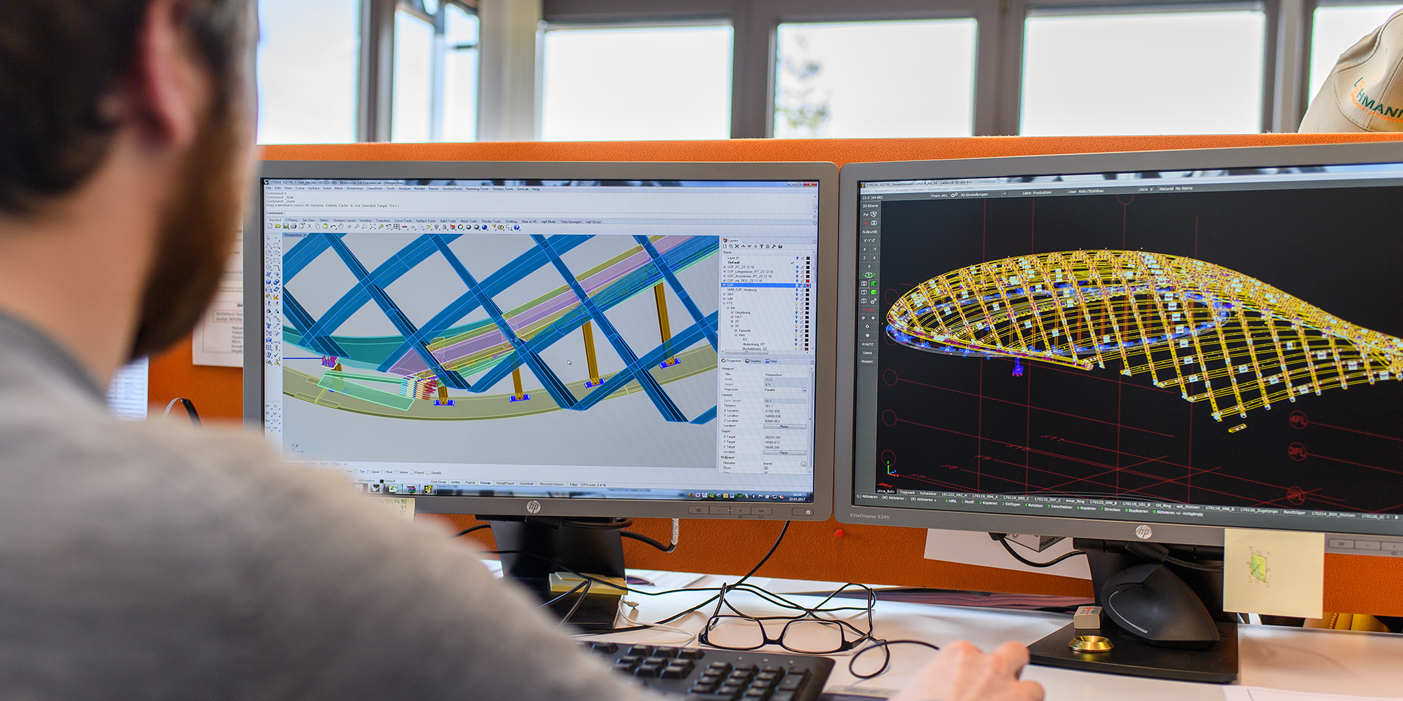 Ein Mitarbeitender sitzt an zwei Bildschirmen und plant am 3D-Modell eines Baus.